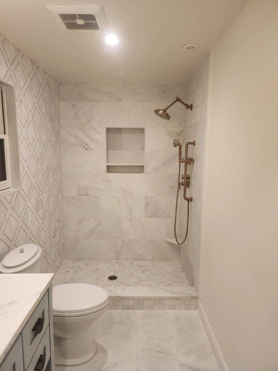 Walk-in shower with marble-look tile, mosaic floor, and bronze rain fixtures — photo published on the Des Limited site